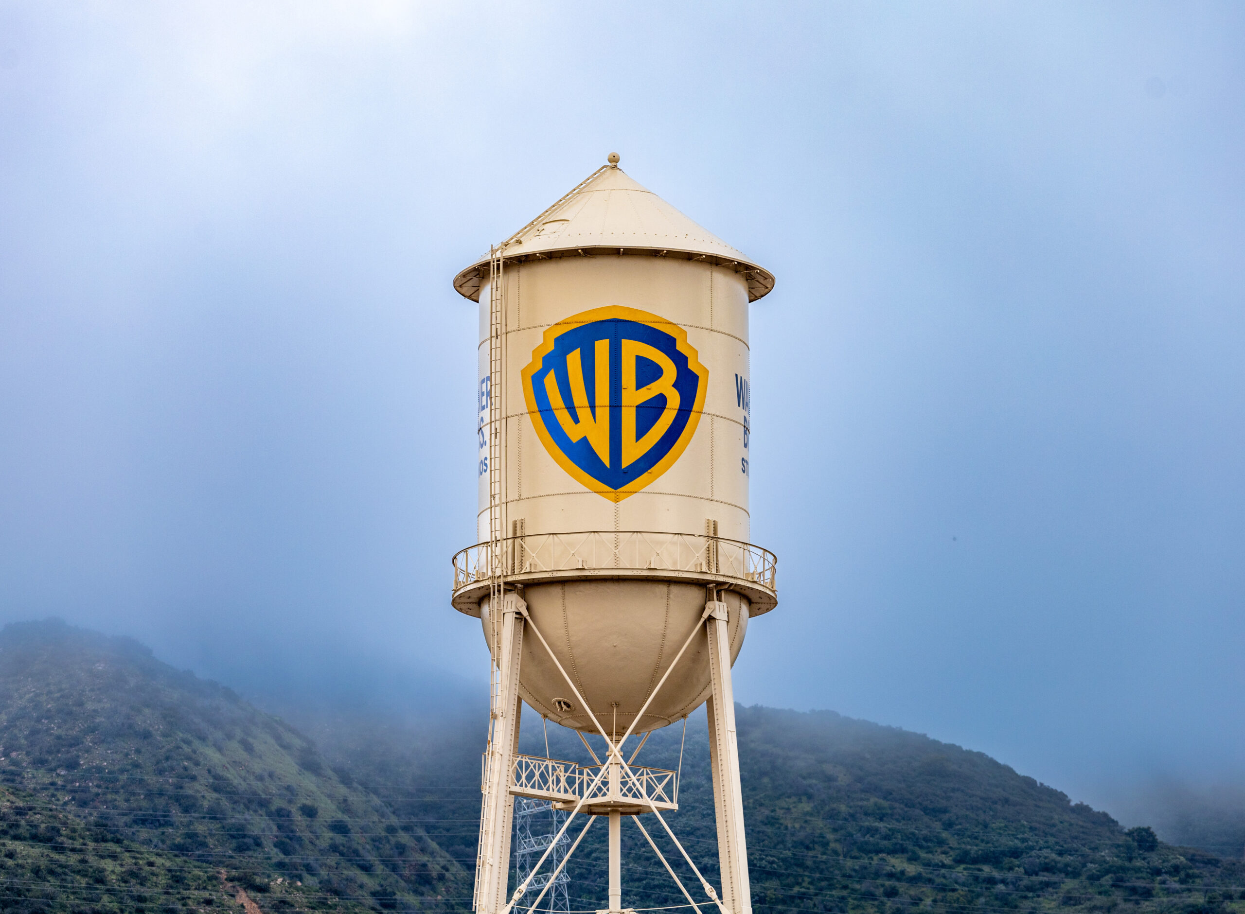 Burbank, USA, Mar 12, 2023 – The iconic Warner Bros. water tower featuring the WB logotype on the studio lot in California, with low clouds and green hills in the background.